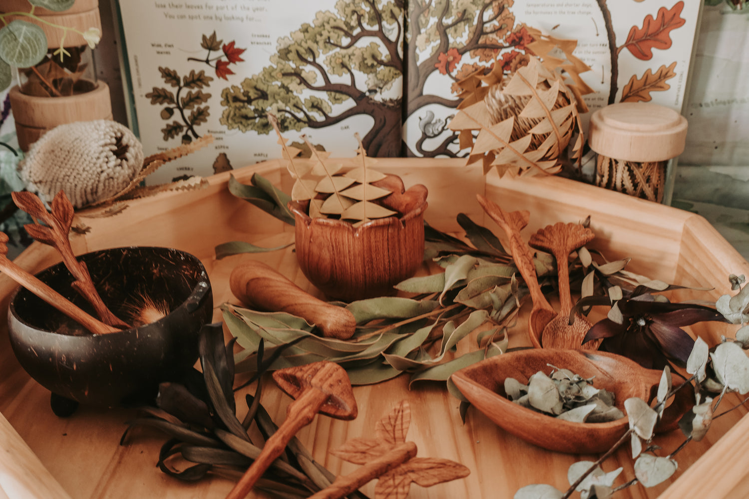 Wooden toys and natural elements on a wooden tray with a nature-themed background.