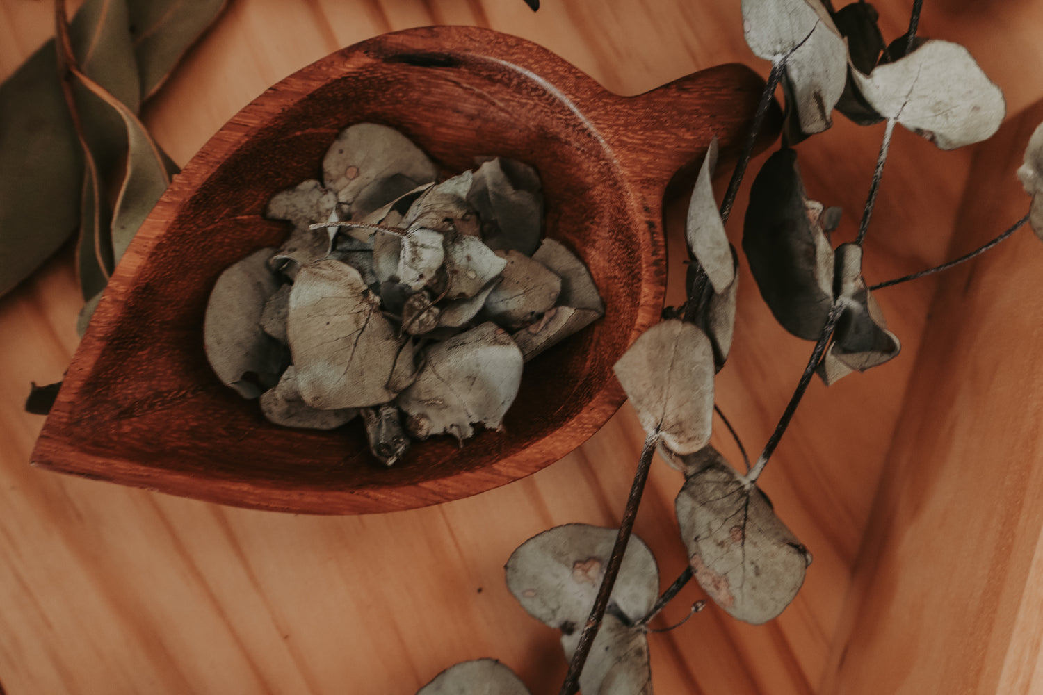 Wooden leaf-shaped bowl filled with dried leaves on a wooden surface