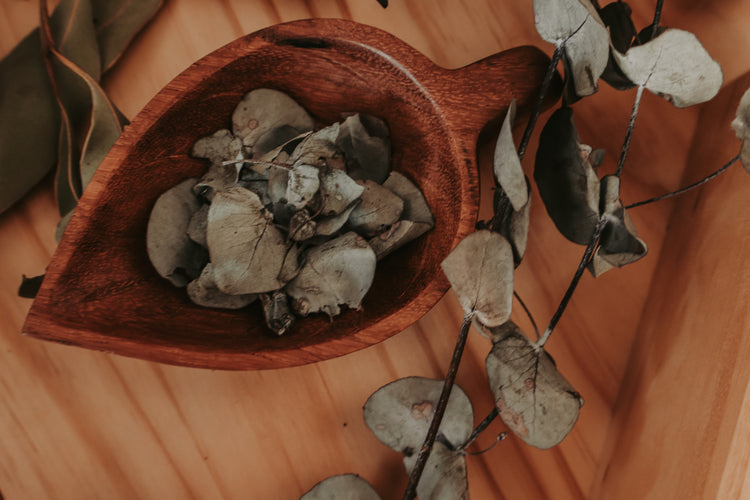 Wooden leaf-shaped bowl filled with dried leaves on a wooden surface